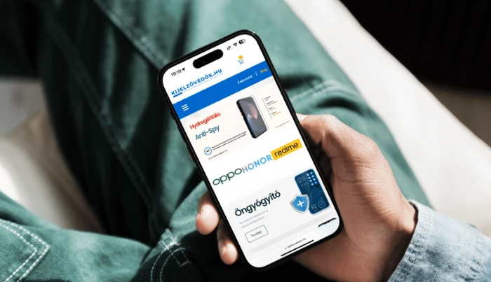 Osoba držící chytrý telefon s maďarským e-shopem Kijelzővédők.hu